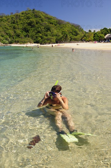 Mexico, Oaxaca, Huatulco, Snorkler adjusting mask while sitting in clear water beside Playa La Entrega. Photo : Nick Bonetti