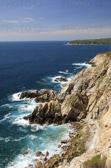 Mexico, Oaxaca, Huatulco, Rocky cliff edge with waves breaking on rocks below and Bahia Maguey. Photo : Nick Bonetti