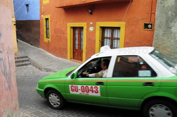 Mexico, Bajio, Guanajuato, Taxi turning down paved street with brightly painted corner houses. Photo : Nick Bonetti