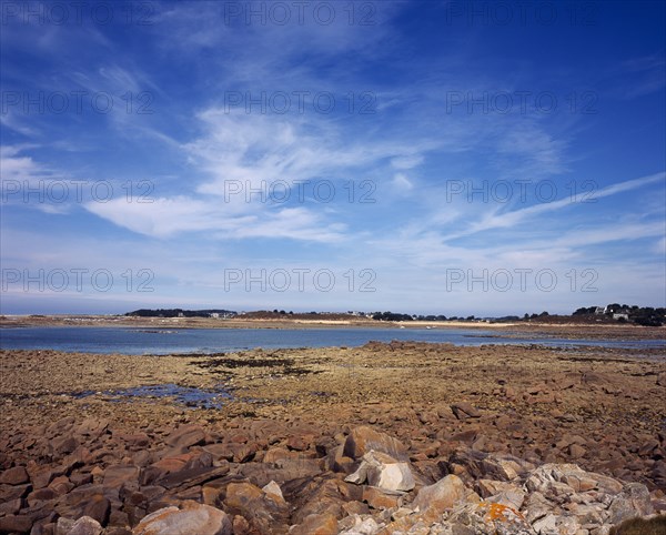France, Cotes d Amor, Brittany, Cote de Granit Rose. Rocky shoreline with view towards Ile Grand on the skyline. Cirrus clouds in blue sky above.. Photo : Bryan Pickering