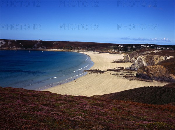 France, Bretagne, Presqu'ile de Crozon, Plage du Veryac'h. Stretch of sandy beach with three figures. Heather clad cliffs in foreground houses and other buildings in far distance. Photo : Bryan Pickering