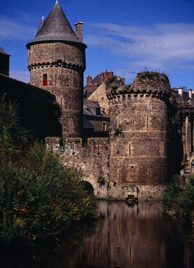 France, Bretagne, Ille-et-Vilaine, Fougeres. Defensive walls and towers of the chateau dating from 11th to15th centuries rising from moat with blue sky beyond. Photo : Bryan Pickering