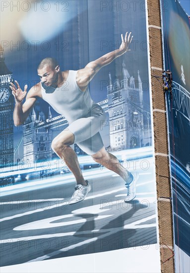 England, London, Stratford A man suspended by rope secures giant hoarding of Gymnast Louis Smith to a building near train station. Photo : Paul Tomlins