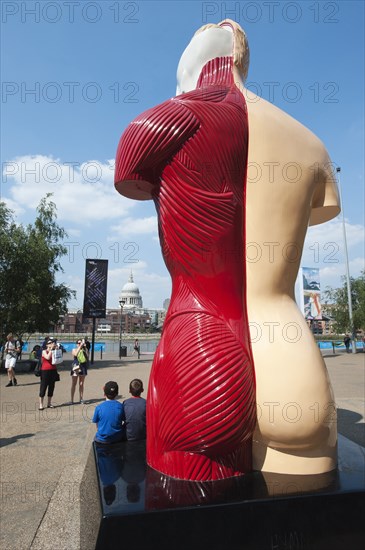 Two children pose for a photograph in front of Damian Hirst's sculpture, 'Hymn', the South Bank, Londonn