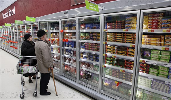 Shopping, Supermarket, Food, Elderly couple with shopping trolley looking at frozen goods in glass fronted freezer displays. Photo : Sean Aidan