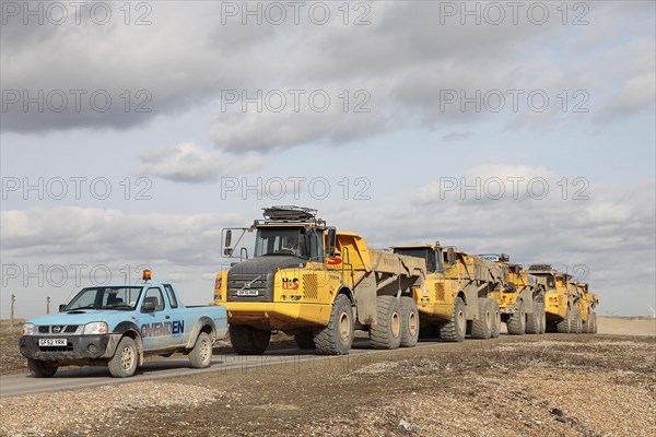Construction, Machines, Tipper Trucks, Convoy of yellow Volvo Dump Trucks used to redistribute pebbles on shingle beach. Photo : Sean Aidan