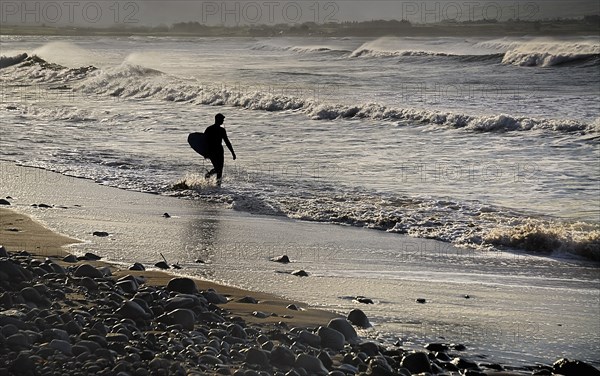 Ireland, County Sligo, Strandhill, Silhouette of surfer with surfboard heading into the sea. Photo : Hugh Rooney