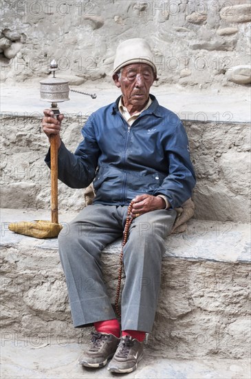 Nepal, Upper Mustang, Lo Manthang, Elderly man praying with prayer wheel in the square near the kings palace. Photo : Sergey Orlov