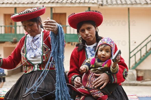 Peru, Indigenous People, Mother and baby in traditional dress with a lady making yarn and infant holding mobile phone. . 
Photo Richard Rickard / Eye Ubiquitous