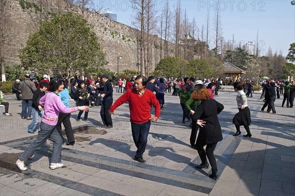 China, Jiangsu, Nanjing, Retired couples dancing beneath the Ming city wall at Xuanwu Lake Park Man in red sweater with arm extended to woman in pink sweater. 
Photo Trevor Page / Eye Ubiquitous