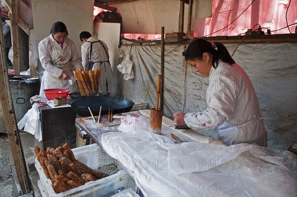 China, Jiangsu, Nanjing, Road-side bakery shop baker cutting strips of dough that will be twisted and deep-fried in a wok to ptoduce Yu Tiao a popular breakfast bread usually eaten with warm soyamilk or porridge or Xi Fan Bundles of Yu Tiao in baskets ready for sale. 
Photo Trevor Page / Eye Ubiquitous