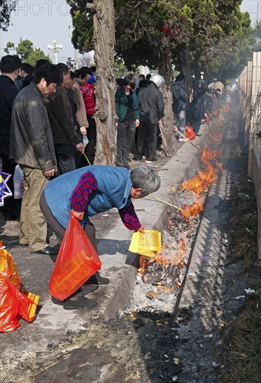 China, Jiangsu, Qidong, Qingming Festival when Chinese people honour their ancestors and deceased family members by visiting their graves or burial grounds to make offerings of fake bank notes and gold ingots which are then burned As the burning of offerings in not allowed inside most cemetries for safety reasons they are burned in the gutter outside. 
Photo Trevor Page / Eye Ubiquitous