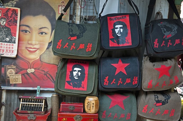 China, Shanghai, Revolutionary kitsch on sale at at Dongtai antique market Chairman Mao Zedong and Che Guevara and Red Star shoulder bags Chinese characters read Serve the People Lin Biao calendar atop Shanghai Belle advertizing poster Fake antique boxes and abacus. 
Photo Trevor Page / Eye Ubiquitous