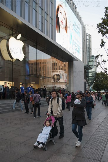China, Shanghai, Modern young Chinese family with daughter in stroller and infant in sling stroll past the Apple store on Nanjing Lu Store staff and Security on steps at entrance evening light. 
Photo Trevor Page / Eye Ubiquitous