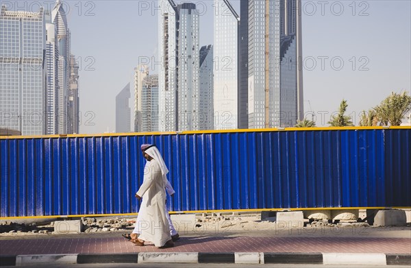 UAE, Dubai, Arab men dressed in tradityional Dishdasha walking past construction site with Sheikh Zayed Road behind. 
Photo John Dakers / Eye Ubiquitous