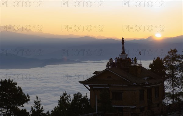 Nepal, Nagarkot, Sunrise view across clouded valley towards Himalayan mountains with Buddhist Stupa on top of building. 
Photo Nic I Anson / Eye Ubiquitous