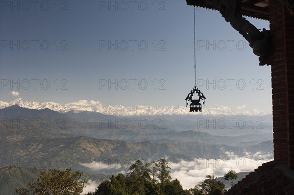 Nepal, Nagarkot, View across clouded valley towards Himalayan mountains wind chime hanging from traditionally carved corner of building in foreground. . 
Photo Nic I Anson / Eye Ubiquitous