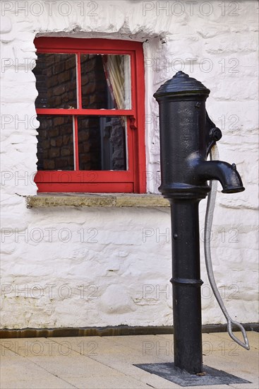 Ireland, North, Derry, Craft Village, Old water pump with small red window in background. 
Photo Hugh Rooney