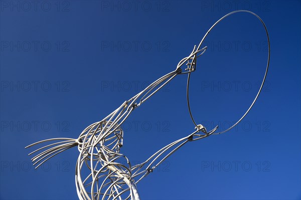 Ireland, North, Belfast, Ring of Thanksgiving sculpture  angular low viewpoint of modern metal sculpture depicting female figure holding up hoop against cloudless blue sky.