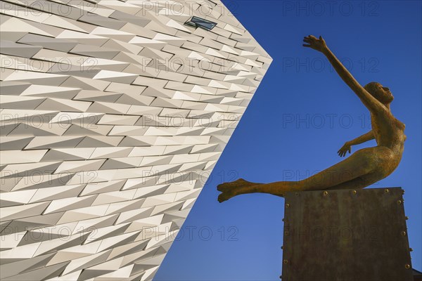 Ireland, North, Belfast, Titanic Quarter, Titanic Belfast Visitor Experience, 'Titanica' sculpture by Rowan Gillespie with a section of the building and blue sky in the background. 
Photo Hugh Rooney