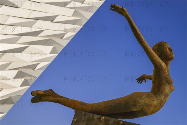 Ireland, North, Belfast, Titanic Quarter  Titanic Belfast Visitor Experience  Titanica sculpture by Rowan Gillespie with a section of the building and blue sky in the background.