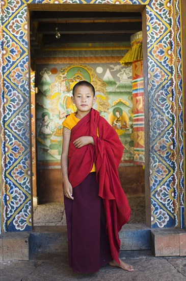 Bhutan, Chimi Lakhang, Young novice monk standing in doorway of Chimi Lakhang temple in the old capital. 
Photo Nic I'Anson