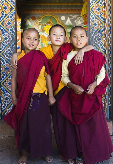 Bhutan, Punakha, Three young novice monks standing in doorway of Chimi Lakhang temple in the old capital. 
Photo Nic I'Anson