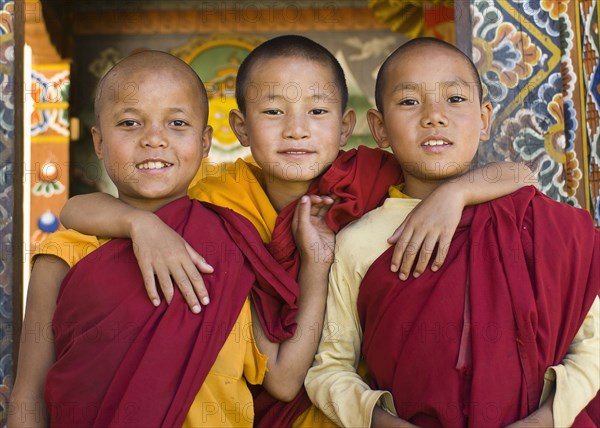Bhutan, Punakha, Three young novice monks standing in doorway of Chimi Lakhang temple in the old capital. 
Photo Nic I'Anson
