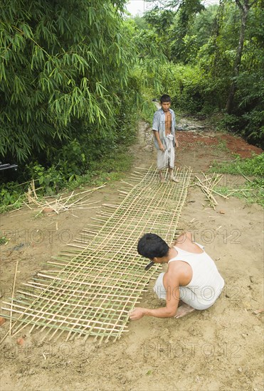 Bangladesh, Chittagong Division, Khagrachari, Two men weaving a large bamboo fence panel. 
Photo Nic I'Anson