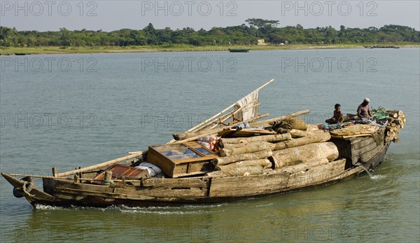 Bangladesh, Industry, Transport, Boat heavily laden with cargo of timber and furniture on river. 
Photo Nic I'Anson