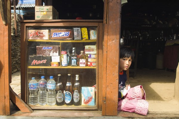 Nepal, Himalayas, Pokhara, Girl sat in a shop doorway on a trekking route with western snacks for sale. 
Photo NIc I Anson