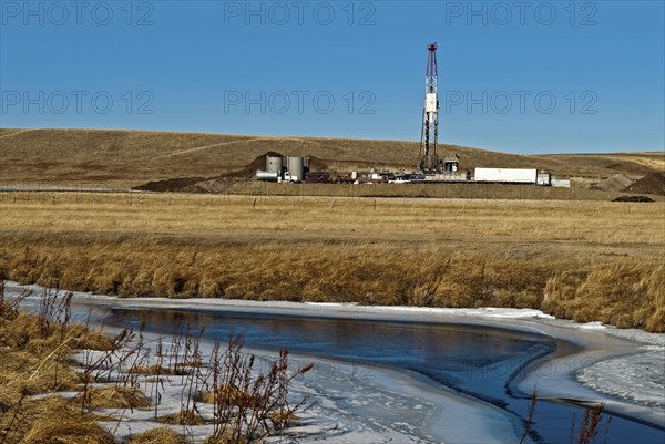 Canada, Alberta, Del Bonita, Fracking near a water source for tight shale oil and gas on the edge of the Bakken play. Ensign Energy of Calgary drilling rig  water storage tanks and road tanker. The water source in the foreground is Shanks Creek which is u