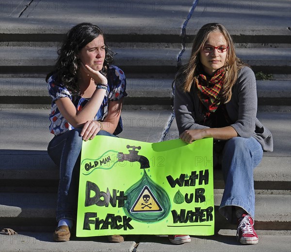 Canada, Alberta, Lethbridge, Two local women atsitting on stone steps at an anti-fracking demonstration holding a green protest sign. Oldman River  which runs through Lethbridge  is the source of the citys water supply.