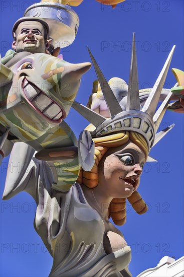 Spain, Valencia Province, Valencia, Papier Mache figure of a woman resembling the Statue of Liberty with another figure flying around her during Las Fallas festival. 
Photo Hugh Rooney