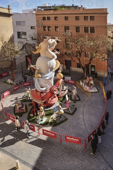 Spain, Valencia Province, Valencia, Papier Mache falla scene with onlookers viewing a giant figure of a lady in the street at Torres de Quart during Las Fallas festival.