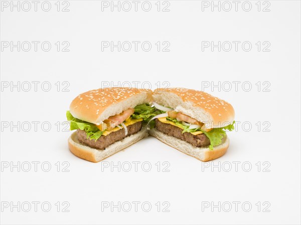 Food, Cooked, Meat, Single cheesburger with salad and tomato ketchup in a bun cut in half and open on a white background.