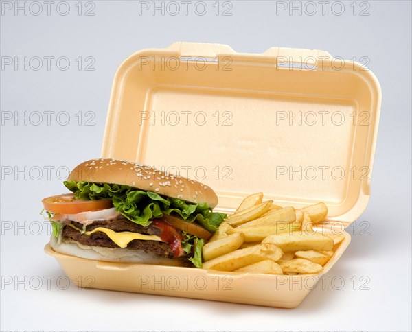 Food, Cooked, Meat, Double cheesburger with salad and tomato ketchup in a bun with potato chips inside a polystyrene foam box on a white background.